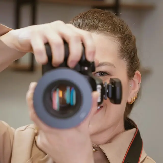 A dra. Francine Lauermann segurando uma câmera fotográfica diante do rosto.