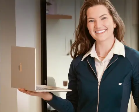 A dra. Francine Lauermann sorrindo, de jaqueta azul-escura, com um notebook aberto na mão.